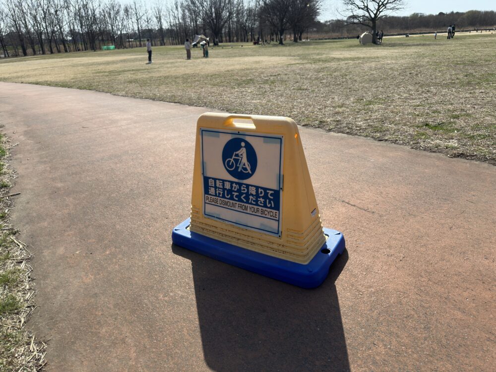 びん沼自然公園の多目的広場の外周園路に置かれている「自転車から降りて通行してください」という注意看板